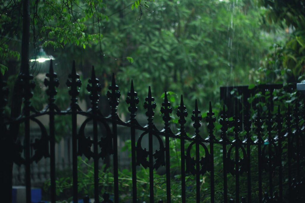 A scenic view of a rain-soaked garden with a decorative metal fence and lush greenery, captured on a moody evening.